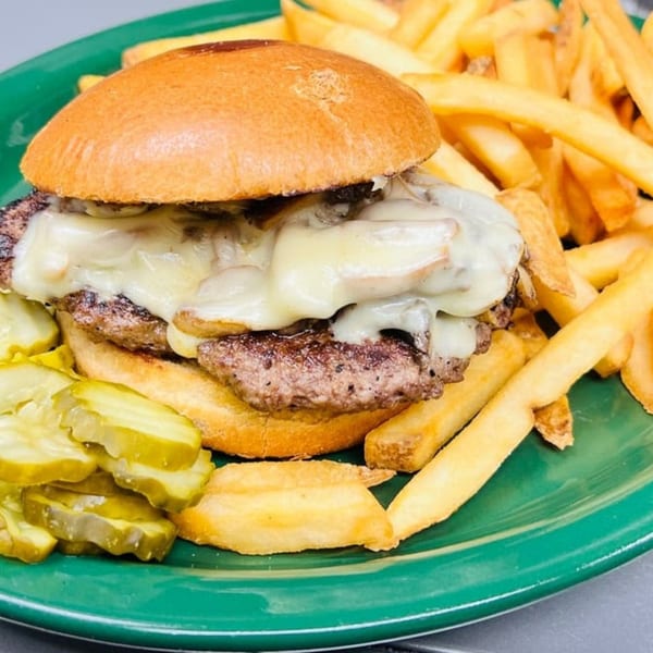 A mushroom swiss burger with fries and pickles on a green plate at Gabriel's Pancake House.