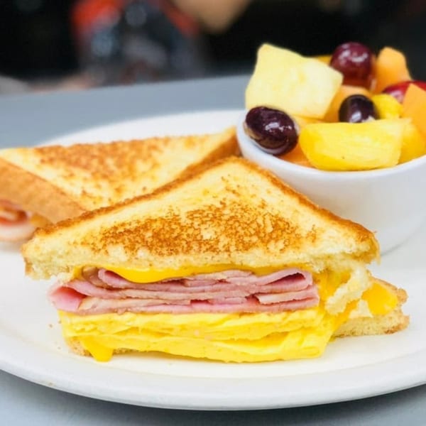 Grilled ham, egg, and cheese sandwich with a side of fresh fruit salad.