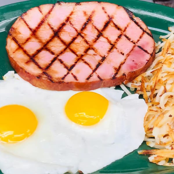 A breakfast plate with grilled ham, two fried eggs, and crispy hash browns on a green plate.