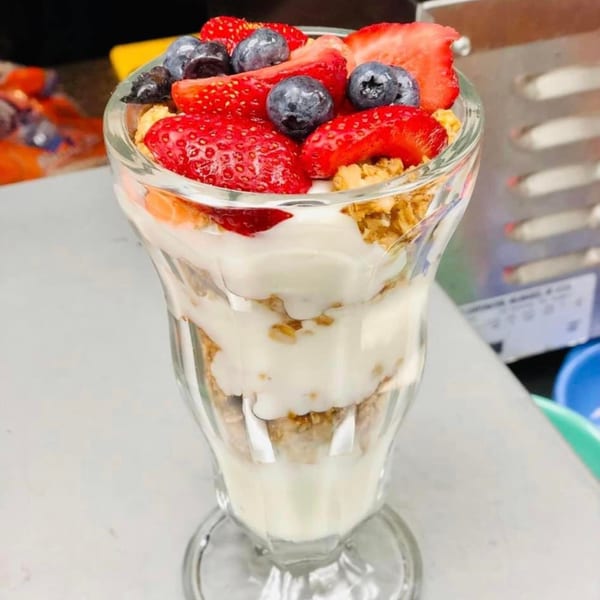 A parfait glass filled with layers of yogurt, granola, strawberries, and blueberries.