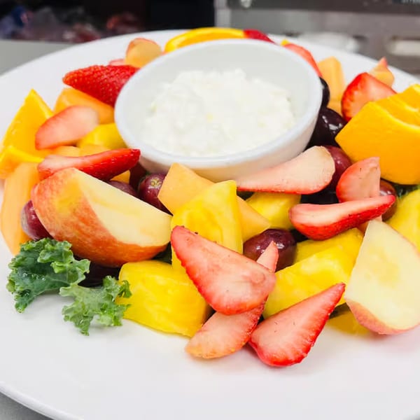 A colorful fruit plate with strawberries, oranges, grapes, apples, cantaloupe, and a side of cottage cheese.