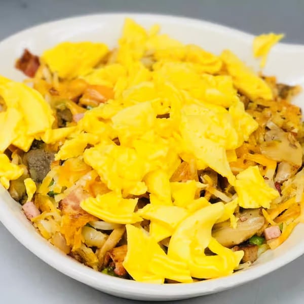 A close-up of a breakfast skillet with scrambled eggs, bacon, sausage, mushrooms, and onions.