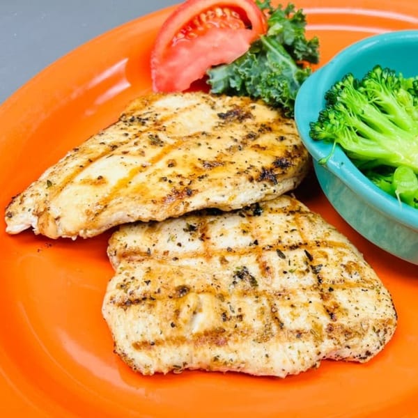 Grilled chicken breasts with broccoli, tomato, and kale on an orange plate.
